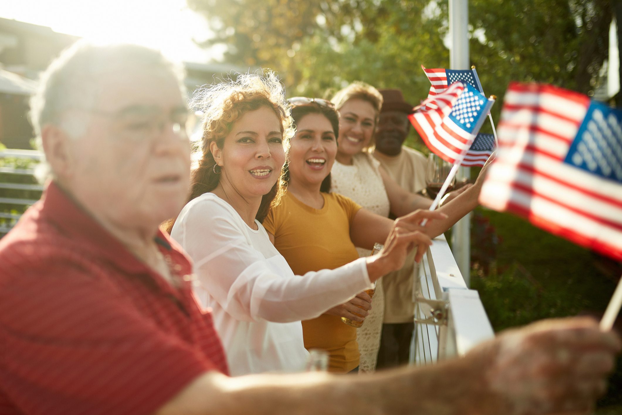 Four seniors happily waving small American flags outdoors.