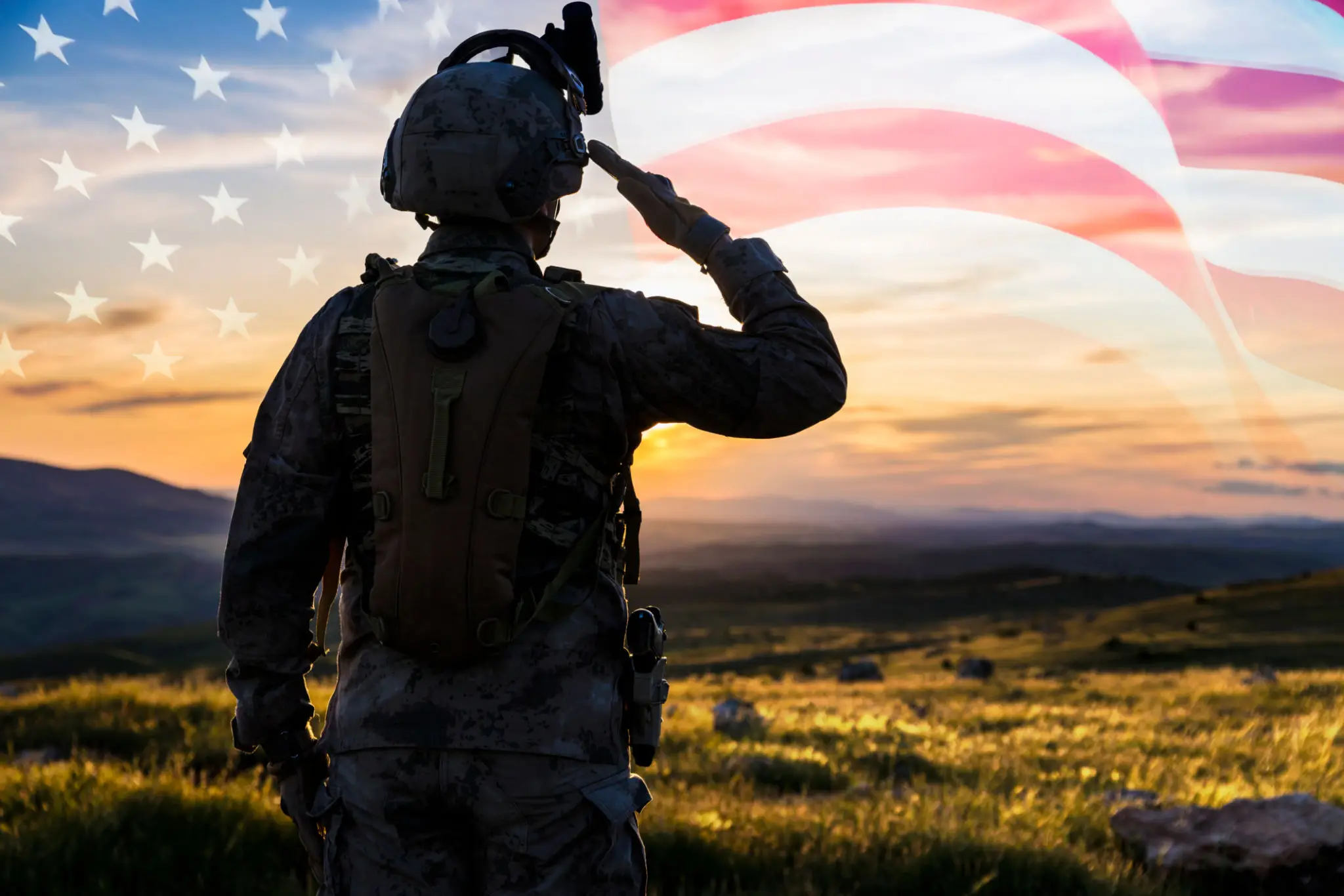A soldier saluting with an American flag backdrop at sunset.
